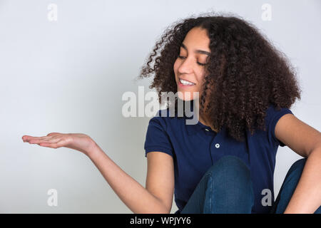 Studio Aufnahme eines biracial Mixed Race African American Girl weibliche Teenager Teenager junge Frau mit lockigem Haar, ihr leere Hand ausgestreckt r Stockfoto