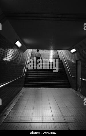 MATSUYAMA, JAPAN - May 30, 2019: ein Graustufen vertikaler einer Person klettern U-Treppe mit Edelstahl Handläufe auf Mauerwerk Stockfoto