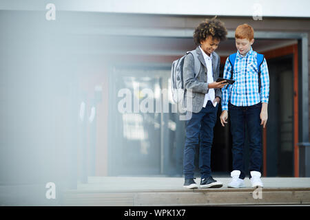 Schule Kinder mit Handy Sie ständigen und etwas aufpassen in der Nähe der Schulgebäude im Freien Stockfoto