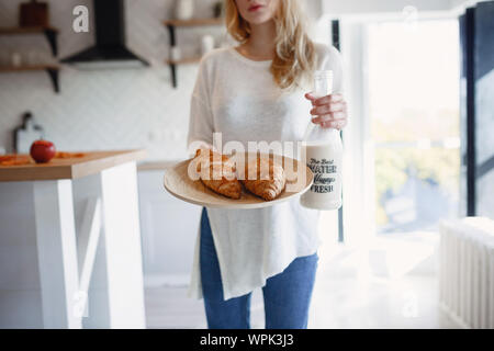 Sseries Herbst in der Küche, Melancholie und warm.. Entspannen in kaltem Wetter. rothaarige Mädchen Holding ein Tablett mit Gebäck und einer Flasche Milch Stockfoto