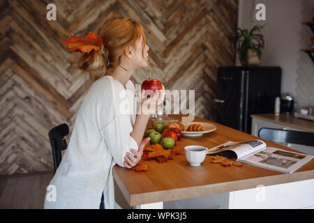 Sseries Herbst in der Küche, Melancholie und warm.. Entspannen in kaltem Wetter. rothaarige Mädchen genießen Äpfel in der Küche Stockfoto