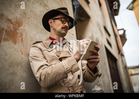 Detektiv schreiben auf einem Notebook während stadning gegen eine alte Mauer Stockfoto