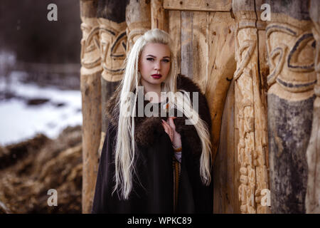 Im freien Porträt der Schönen wütend skandinavischen Krieger Ingwer Frau in traditioneller Kleidung mit Pelzkragen, mit Schwert in der Hand und Holz- V Stockfoto