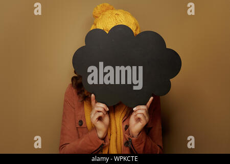 Hallo Herbst. moderne Frau in gelb Baskenmütze und Schal Verstecken hinter Cloud Form leere Tafel auf beigem Hintergrund. Stockfoto