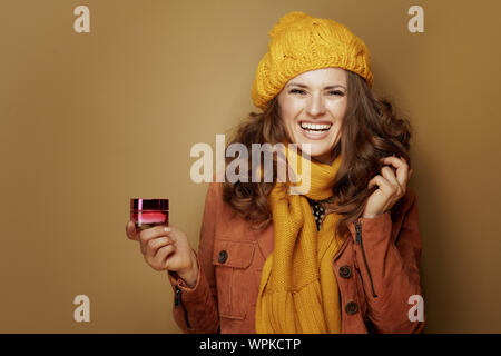 Hallo Herbst. Portrait von Happy stilvolle Frau in gelb Baskenmütze und Schal mit jar Gesichts Creme auf Bronze Hintergrund isoliert. Stockfoto