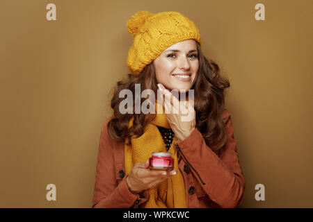 Hallo Herbst. Porträt der glückliche junge Frau in gelb Baskenmütze und Schal mit Gesichts Creme auf braunem Hintergrund. Stockfoto