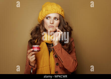 Hallo Herbst. Portrait von Betroffenen 40 Jahre alte Frau in gelb Baskenmütze und Schal mit jar Gesichts Creme gegen beigen Hintergrund. Stockfoto