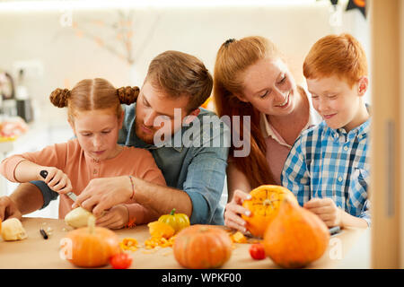 Glückliche Familie mit zwei Kindern am Tisch sitzen und die Vorbereitung der Reife Kürbisse für Halloween zusammen zu Hause Stockfoto
