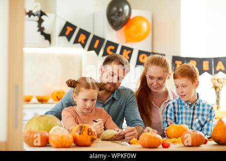 Glückliche Familie mit zwei Kindern am Tisch sitzen und die Fertigkeiten von kürbisse sie zusammen die Vorbereitung für Halloween Party Stockfoto