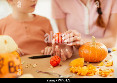 In der Nähe von Frau tun Kunst zusammen mit kleinen Mädchen sie verzieren kleine Kürbisse am Tisch Stockfoto