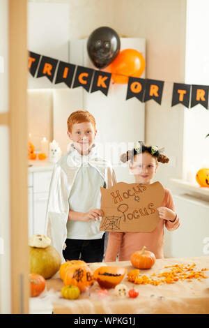 Porträt von zwei Freunden in Kostüme gekleidet, Plakat und Kamera beim stehen im Zimmer dekoriert für Halloween Stockfoto