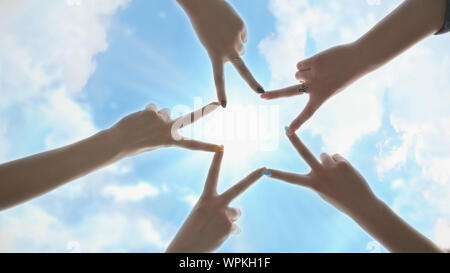 Menschen, die sternförmig mit den Fingern gegen den blauen Himmel mit leuchtenden Strahlen der Sonne. Stockfoto