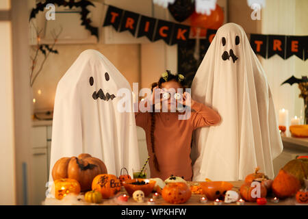 Portrait von kleinen Mädchen mit unheimlichen Augen stehen zwischen ihren Freunden in Ghost Kostüme sie Spaß an Halloween Party Stockfoto