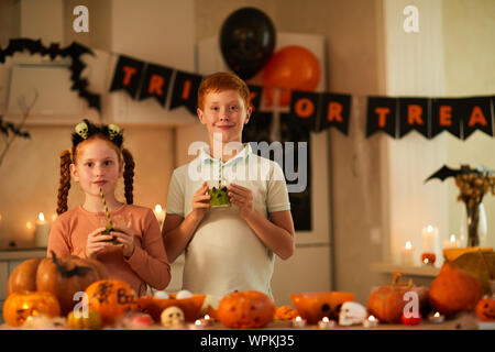 Porträt von zwei Freunde halten Gläser mit Saft und trinken Sie aus trinkhalm während der Halloween Party zu Hause Stockfoto