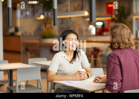 Glückliche junge Frau trinkt Kaffee und das Gespräch mit dem jungen Mann, während Sie am Tisch sitzen und Diskutieren, die Momente im Cafe Stockfoto