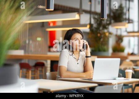 Junge Frau hat einen Anruf am Tisch mit Laptop und trinken Kaffee im Restaurant sitzen Stockfoto