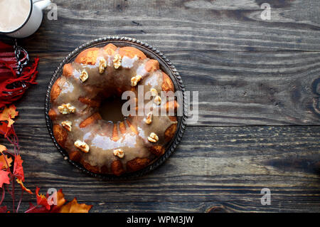 Lecker, Pumpkin Spice Bundt Cake mit braunem Zucker Zuckerguss und Walnüsse mit Herbstlaub und Kaffee über einen rustikalen Holztisch Hintergrund mattiert. Stockfoto