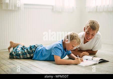 Teenager auf dem Boden liegend seinen jüngeren Bruder helfen bei den Hausaufgaben. Stockfoto