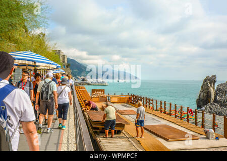 Touristen zu Fuß entlang der Küste der Spiaggia di Fegina, der Sandstrand als Werke in Monterosso al Mare, in der Cinque Terre, Italien Stockfoto