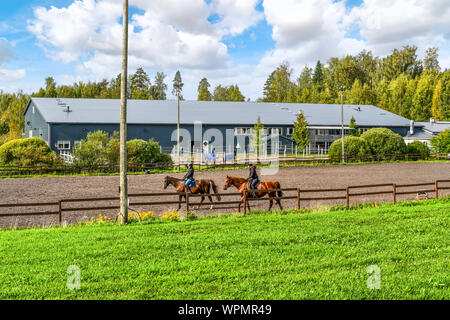 Zwei weibliche Reiter reiten rassigen Pferden auf einer Pferdefarm vor einem großen Indoor Pferd Arena an der Stadt von sipoo Finnland Stockfoto