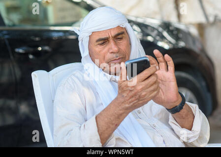 Muslimische älterer Geschäftsmann mit einem Smart Phone. Alte arabische Menschen in traditionellen Kopf Kleidung Outdoor Portrait. Stockfoto