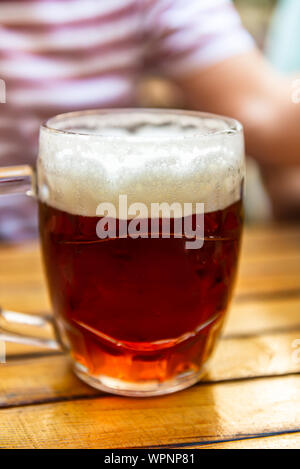 Der Mensch ist ein frisch gezapftes Glas Bier in der Hand Stockfoto