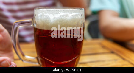 Der Mensch ist ein frisch gezapftes Glas Bier in der Hand Stockfoto