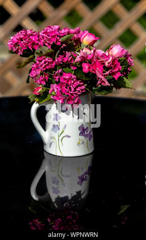 Ein Krug mit rosa Rosen und Hortensien Blumen auf schwarzem Glas Tisch. Stockfoto