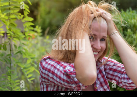 Lachende junge Frau in kariertem Hemd bekleidet hält sich die Hand vor den Kopf. Stockfoto