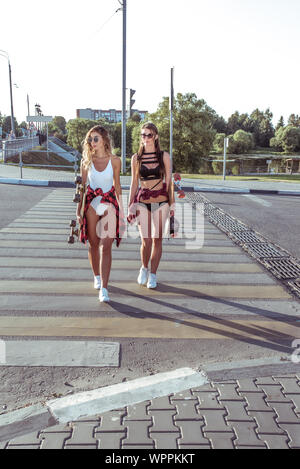 Zwei Freundinnen Spaziergang im Sommer in der Stadt, im Hintergrund die Straße überqueren, Badebekleidung, Shorts und Baseball Caps, Skateboard lange Sonnenbrille. Wochenende gehen Stockfoto