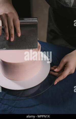 Konditor richtet die Creme mit einem Spachtel. Der Meister der Kuchen Linien die Creme auf einem beigen Hochzeitstorte Stockfoto