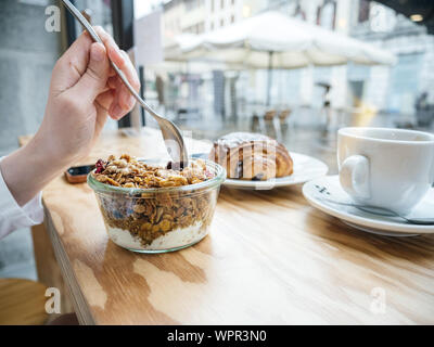 In der Nähe der seitlichen Blick auf Frau essen leckeren Joghurt mit Müsli Trinkwasser in den frühen Morgenstunden in französischer Sprache Cafe Stockfoto