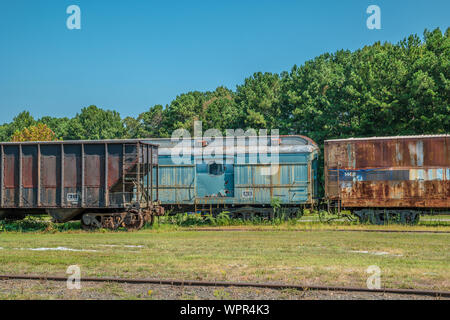 Rost- und verfallende Eisenbahn Waggons und einem Trichter links an den Anschlüssen in einem verwilderten Feld an einem sonnigen Tag im Sommer verlassen Stockfoto