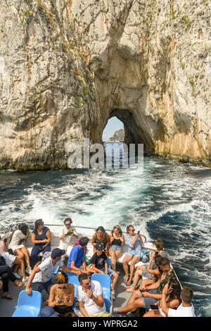 Insel Capri, Italien - AUGUST 2019: Menschen auf der Rückseite des ein Boot, das durch die Faraglioni Felsen an der Küste von Capri bestanden hat. Stockfoto