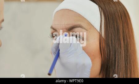 Das Mädchen Kosmetikerin Markierungen mit Hilfe eines Bleistifts die Zukunft Tattoo von Augenbrauen. Stockfoto