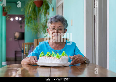 Ältere faltige Frau sitzt und ein Kuchen auf dem Tisch Stockfoto