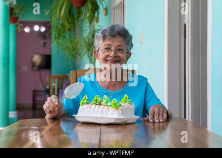 Ältere faltige Frau sitzt und ein Kuchen auf dem Tisch Stockfoto