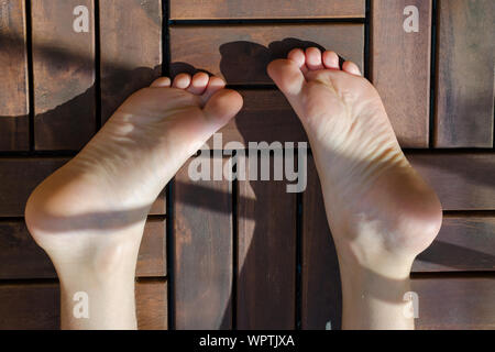 Kind Füße close-up auf dem Holzboden auf dem Balkon auf sonnigen Tag. Das Kind auf dem Holzboden. Stockfoto