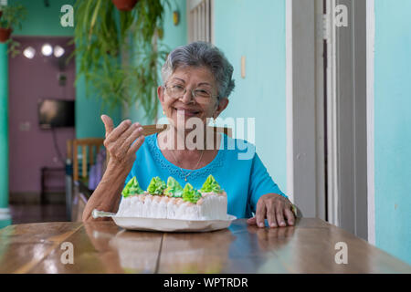Ältere faltige Frau sitzt und ein Kuchen auf dem Tisch Stockfoto