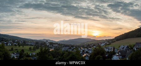 Weiten Panoramablick über die bergige Dorf von Grafschaft im Winter Sport Region Sauerland, Deutschland, während ein farbenfroher Sonnenuntergang Stockfoto