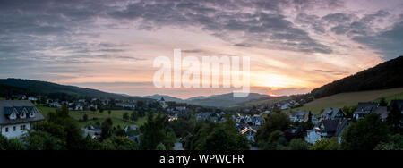 Weiten Panoramablick über die bergige Dorf von Grafschaft im Winter Sport Region Sauerland, Deutschland, während ein farbenfroher Sonnenuntergang Stockfoto