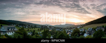 Weiten Panoramablick über die bergige Spa Village von Grafschaft im Winter Sport Region Sauerland, Deutschland, bei Sonnenuntergang mit einer teilweise colo Stockfoto