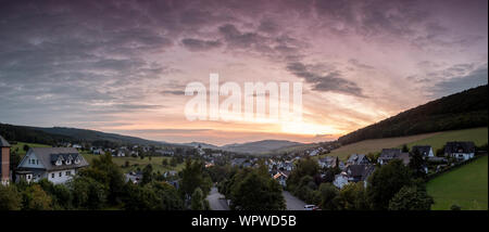 Weiten Panoramablick über die bergige Dorf von Grafschaft im Winter Sport Region Sauerland, Deutschland, während ein farbenfroher Sonnenuntergang Stockfoto