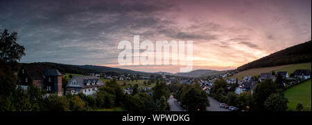 Weiten Panoramablick über die bergige Dorf von Grafschaft im Winter Sport Region Sauerland, Deutschland, während ein farbenfroher Sonnenuntergang Stockfoto