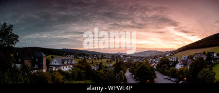 Weiten Panoramablick über die bergige Dorf von Grafschaft im Winter Sport Region Sauerland, Deutschland, während ein farbenfroher Sonnenuntergang Stockfoto