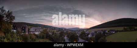 Weiten Panoramablick über die bergige Dorf von Grafschaft im Winter Sport Region Sauerland, Deutschland, während ein farbenfroher Sonnenuntergang Stockfoto