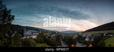 Weiten Panoramablick über die bergige Dorf von Grafschaft im Winter Sport Region Sauerland, Deutschland, während ein farbenfroher Sonnenuntergang Stockfoto