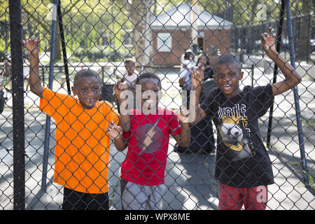 Die jährlichen Universal Hip Hop Parade für Soziale Gerechtigkeit statt zu Ehren von Marcus Garvey in der Bedford Stuyvesant Nachbarschaft von Brooklyn, New York. Jungen auf einem lokalen Spielplatz beobachten die Parade durch. Stockfoto