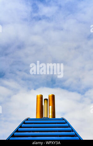 Einfache grafische Vorderansicht der rostigen Schiff Auspuffrohre und blaue Verkleidung gegen den blauen Himmel mit Wolken. Stockfoto