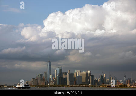 Eine hohe wolkenbildung Zwerge downtown Manhattan, New York in diesem Blick von Brooklyn, NY. Ein NYC Fähre Geschwindigkeiten in Richtung East River. Stockfoto